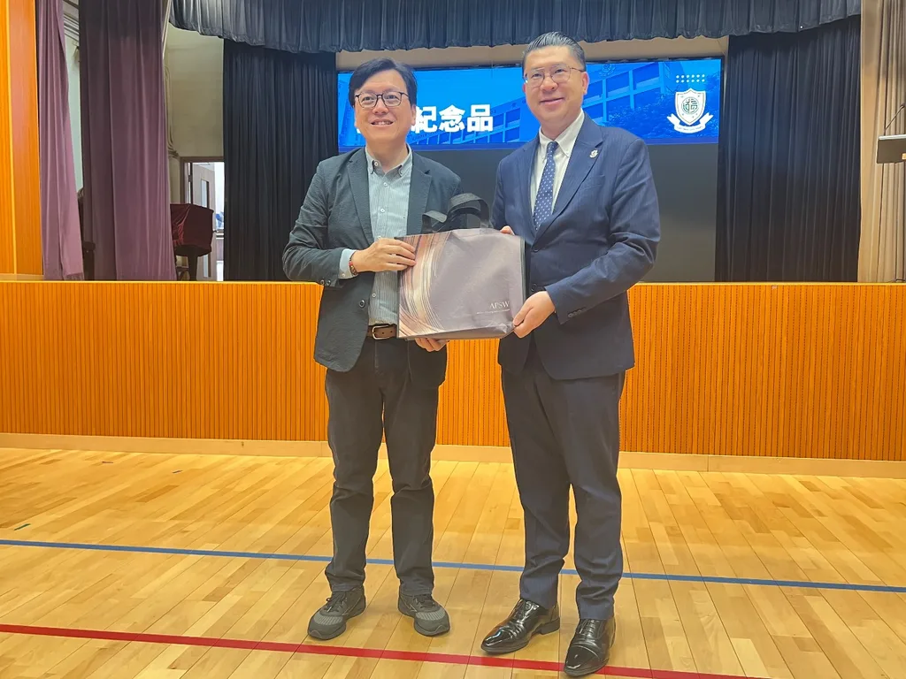 兩位男士在台上共同手持一個印有「AFSW」字樣的禮袋,背後藍色屏幕顯示「紀念品」及白色校徽。
